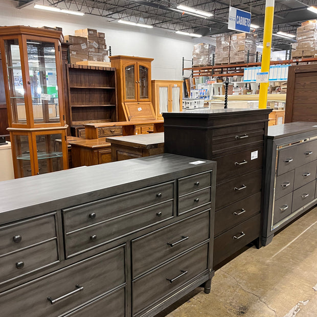 Large dark wooden dresser in a warehouse setting with other furniture in the background.