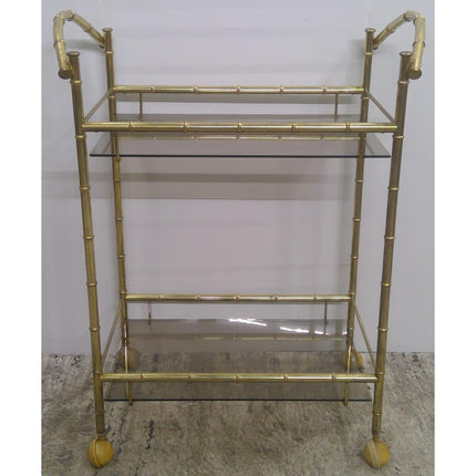 Gold metal bar cart with glass shelves on a plain background