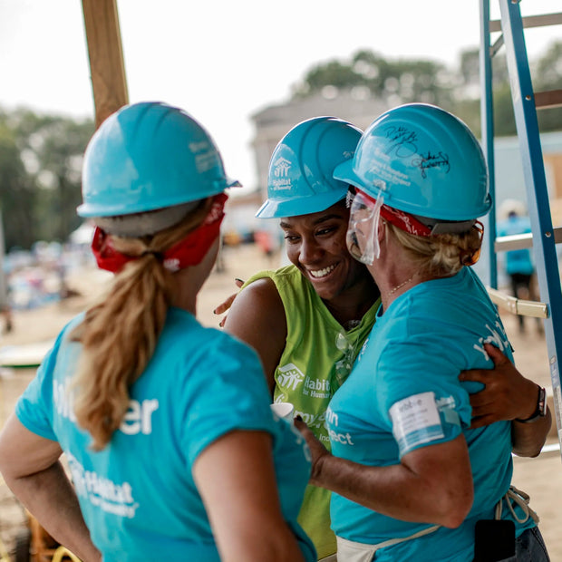 Three women in blue hard hats and shirts standing together on a construction site.