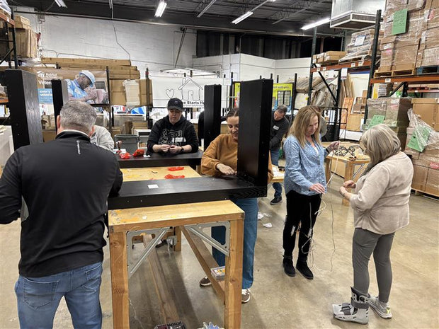 Group of people in Addison ReStore (warehouse setting) assembling black console tables
