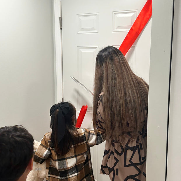 Person with a patterned dress standing in front of a door cutting a red ribbon.