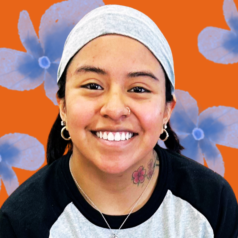 Person wearing a gray headscarf with and black and white baseball tee against a blue and orange floral background