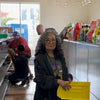 Woman in Oak Forest ReStore setting wearing a Habitat for Humanity shirt. She's holding a plastic yellow bin and smiling, with men working in the background.
